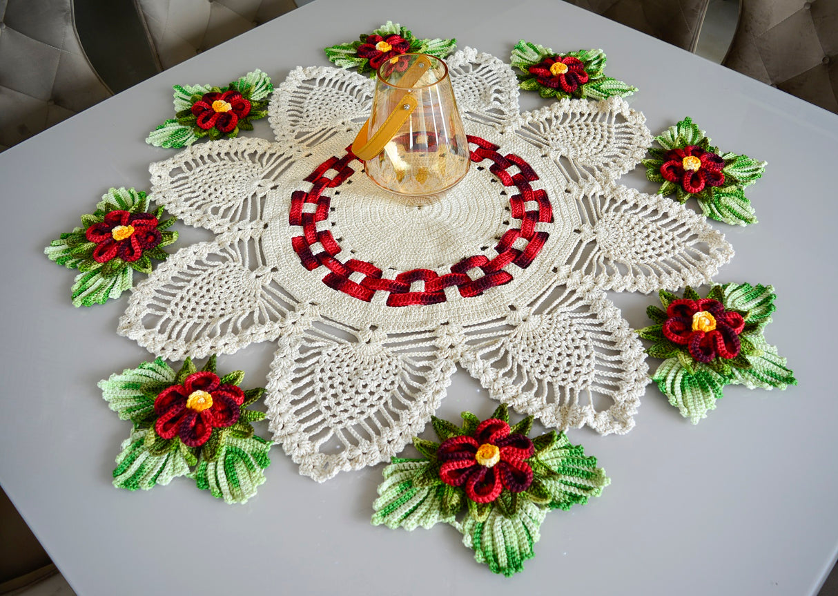 Circulo Barroco Natural Brilho - Natural Cotton Yarn Gold/Silver, 657m / 433m, 400g - A crocheted holiday table runner or doily set on a gray table, featuring white lace petals with red and green poinsettia flowers and a central red-and-black pattern, with a small glass bottle placed on top.