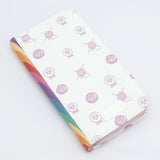 KnitPro Symfonie 2 double pointed needle set, 20 cm - A zippered wallet or planner cover with a white background decorated with light purple yarn and sheep illustrations, featuring a vibrant rainbow-colored striped spine.