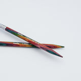 KnitPro Symfonie 2 fixed circular knitting needles with swivel cable, 60 cm - Two wooden knitting needles with a colorful, marbled pattern of red, green, and orange, crossed on a plain white background. The brand name 'Kreft' is printed in white on the shafts.