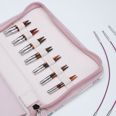 KnitPro Symfonie 2 Mini interchangeable needle set, 5 cm - A pink zippered carrying case holding multiple knitting needles arranged in elastic loops. The needles have silver metal shafts and tips with multicolored yarn wrapped around them.